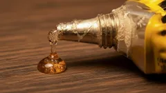 Bico de pistola de cola quente com gota de cola sobre superfície de madeira.