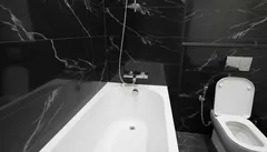 Casa de banho moderna com banheira branca e paredes de mármore preto, sanita ao fundo.