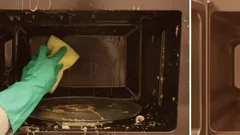 Pessoa a limpar um micro-ondas sujo com esponja e luva de borracha verde.