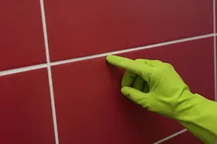 Mão com luva verde limpa juntas de azulejos vermelhos na casa de banho ou cozinha.