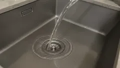 Água a correr numa pia de cozinha em inox com ralo ao centro.