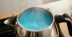 Chaleira elétrica com água azul a ferver e vapor a sair na cozinha.