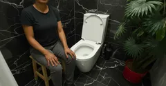 Casa de banho moderna com sanita branca e pessoa sentada num banco ao lado