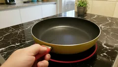 Pessoa segurando frigideira sobre fogão de indução numa cozinha moderna.