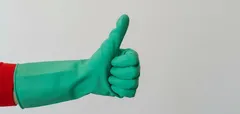 Mão com luva de limpeza verde fazendo sinal de positivo em fundo branco.
